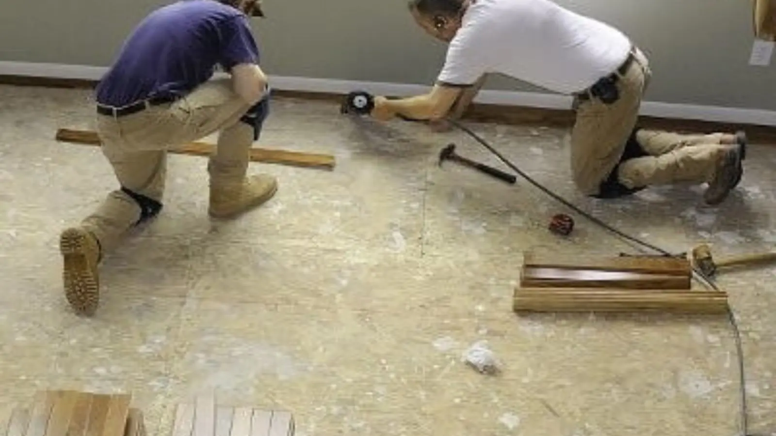 Two workers kneeling on a subfloor during water damage repair and floor rebuilding